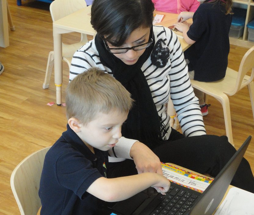 A teacher and student using a laptop on a desk at Meadow Montessori School in South Richmond, TX