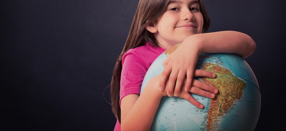 A smiling girl wrapping her arms around a globe