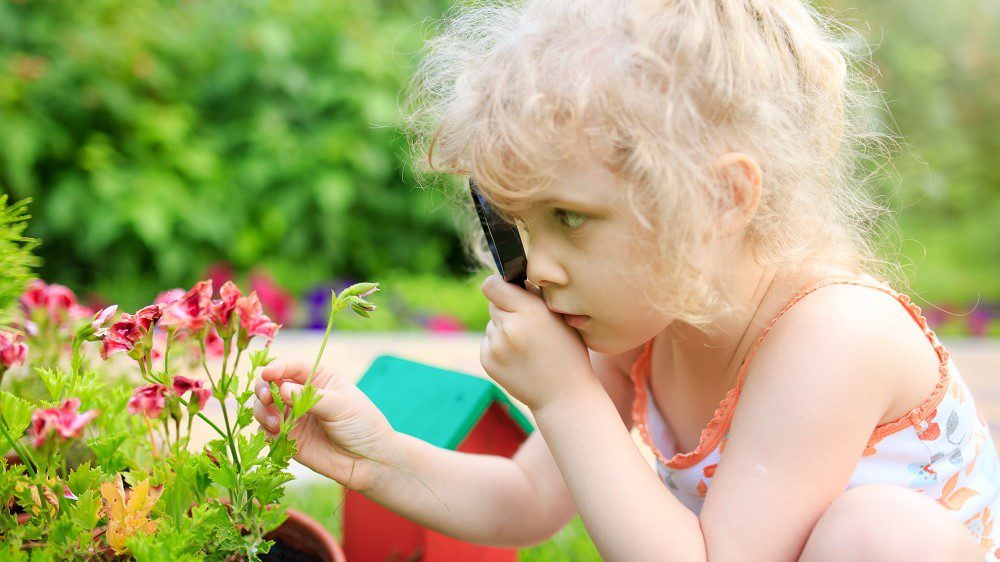 A young girl using a magnifying glass to examine some pink flowers