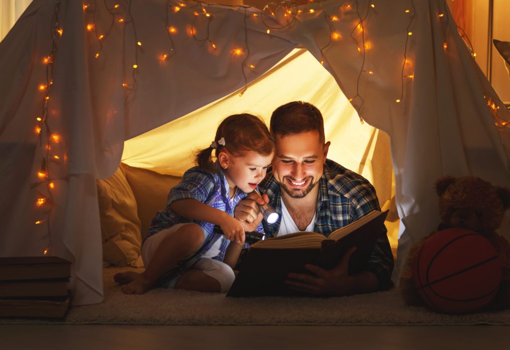 A father reading a book via a flashlight to his daughter