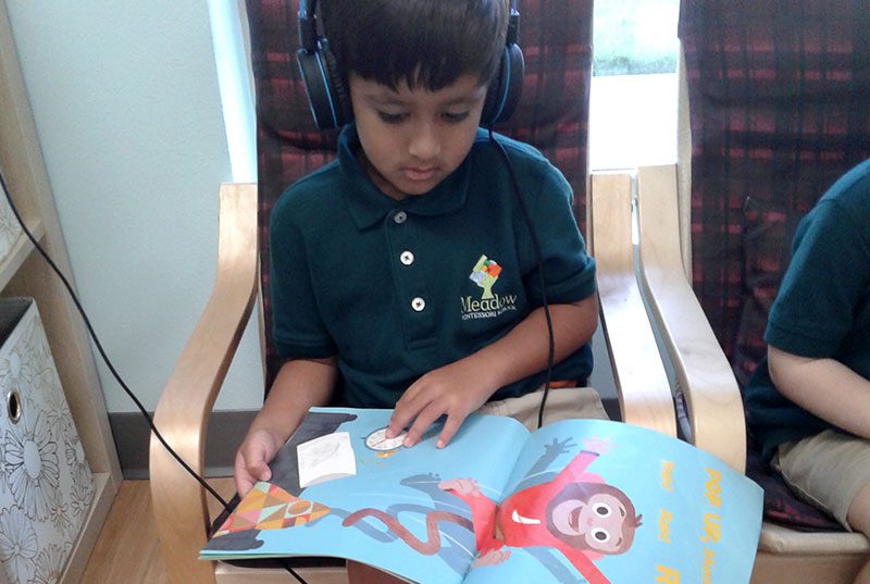 A student listneing to a book and following along at Meadow Montessori School in South Richmond, TX