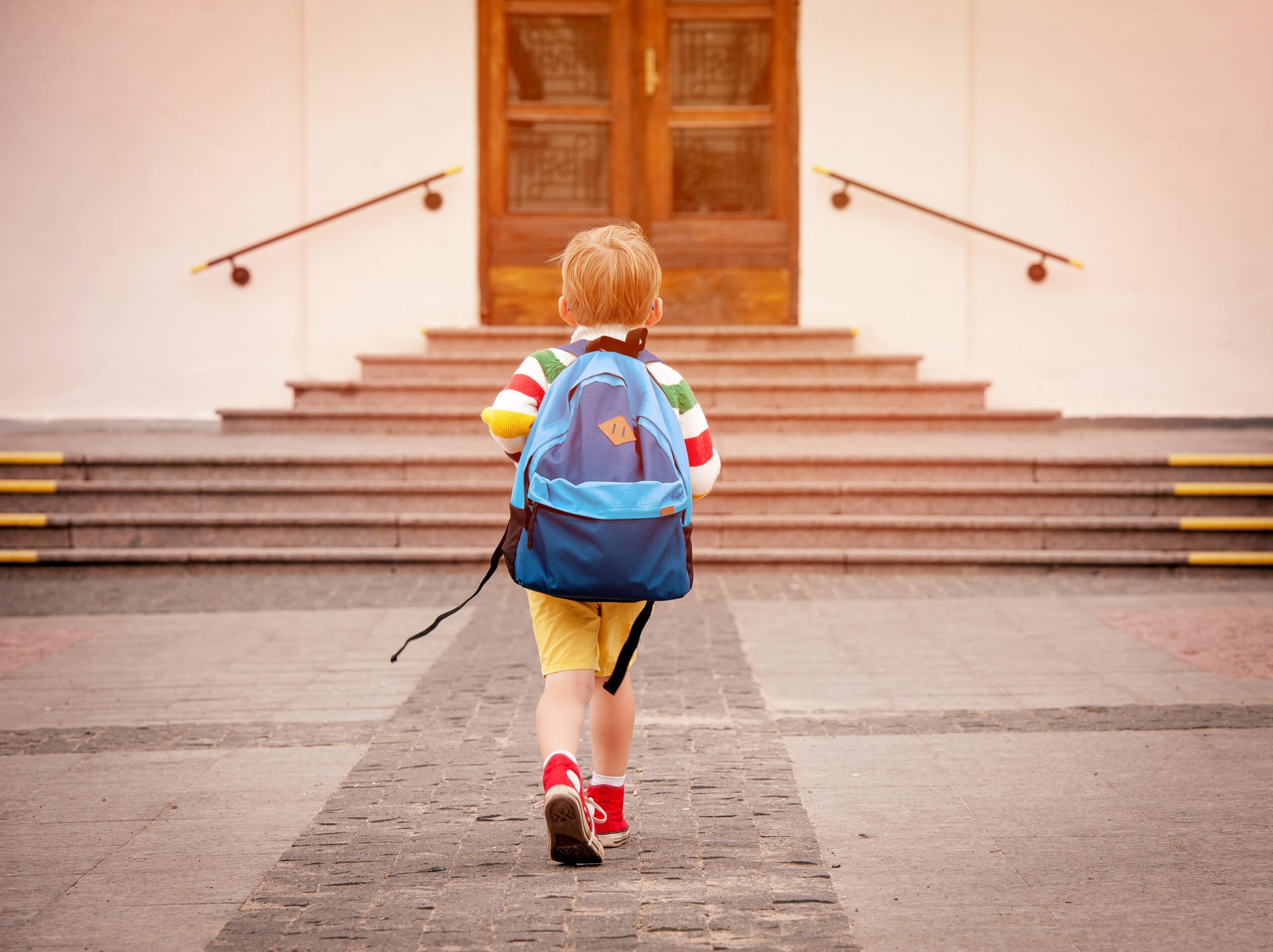A student with backpack walking up steps towards a wooden door