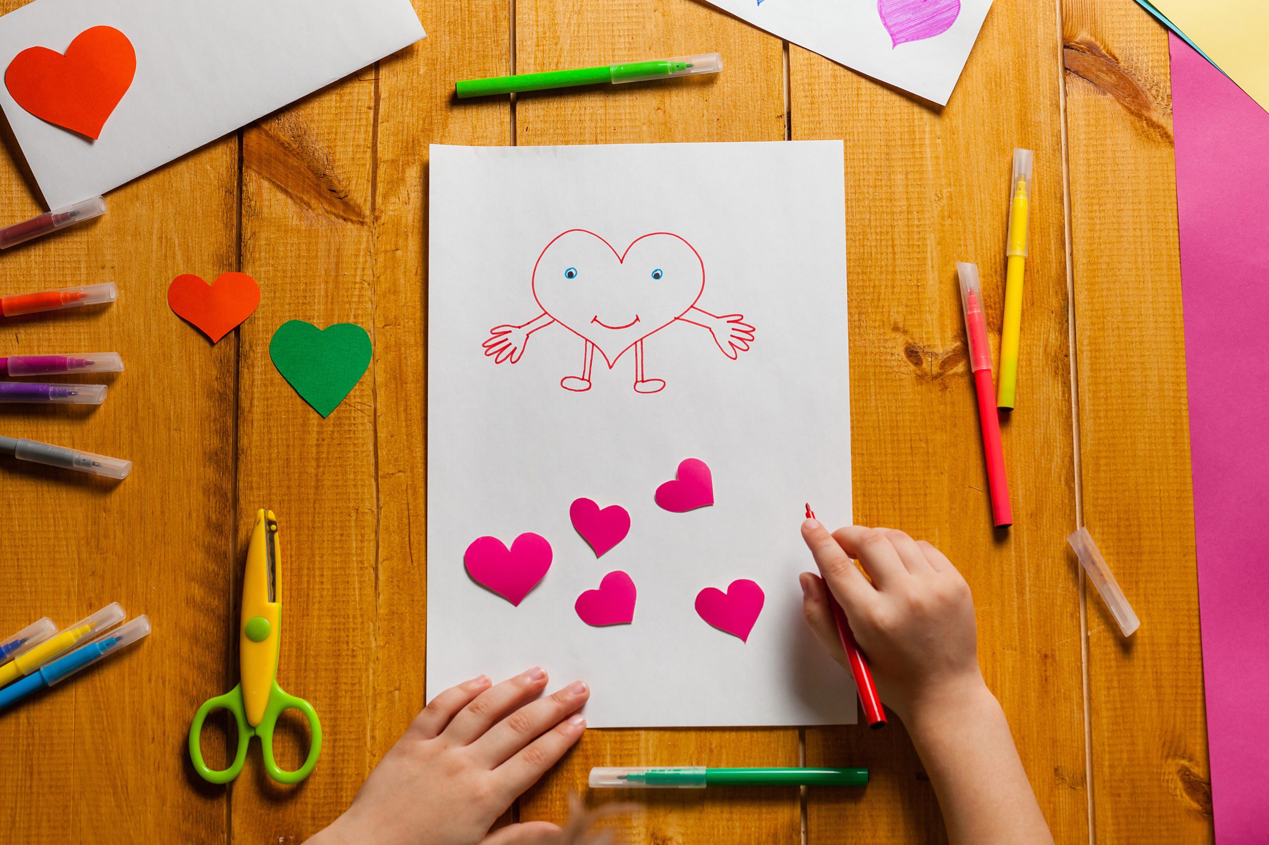 A child drawing a heart and five paper hearts
