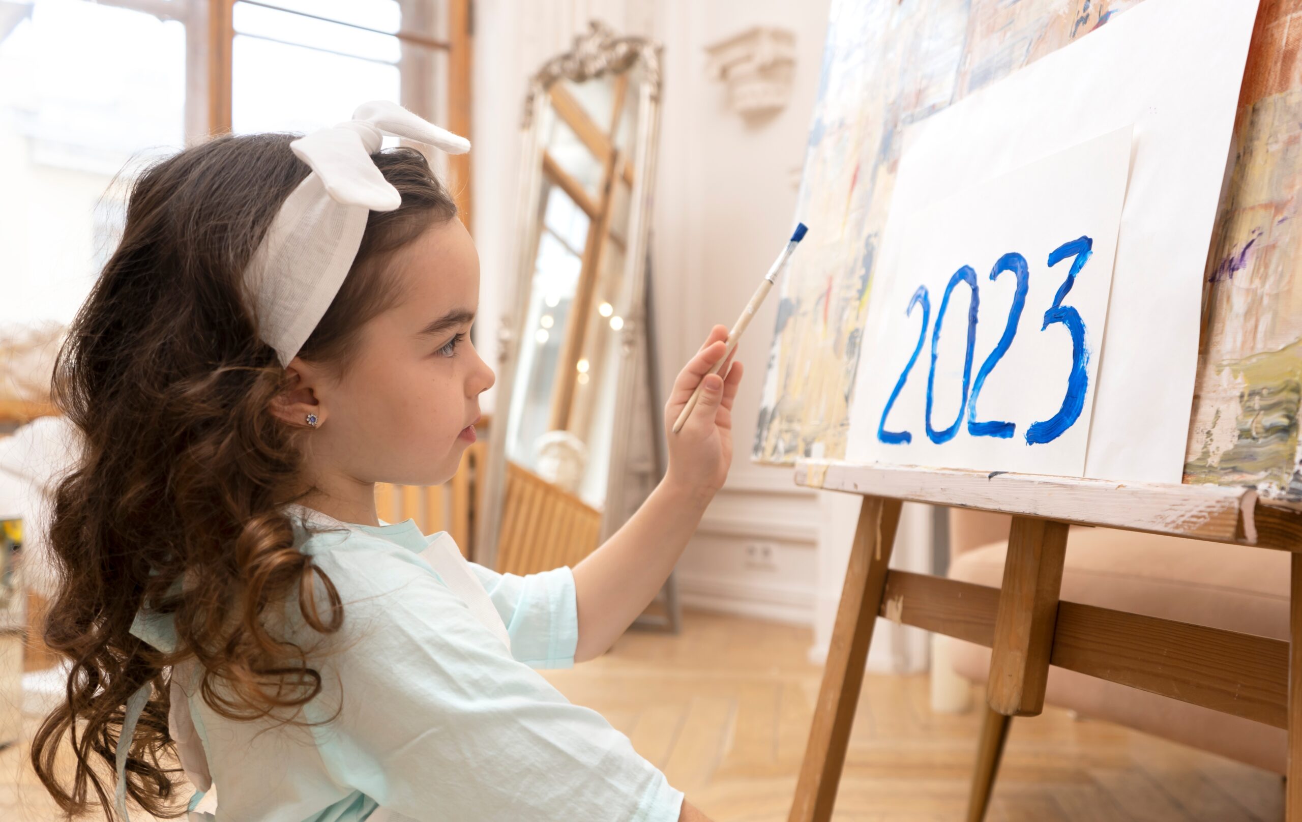 young girl painting 2023 on an easel